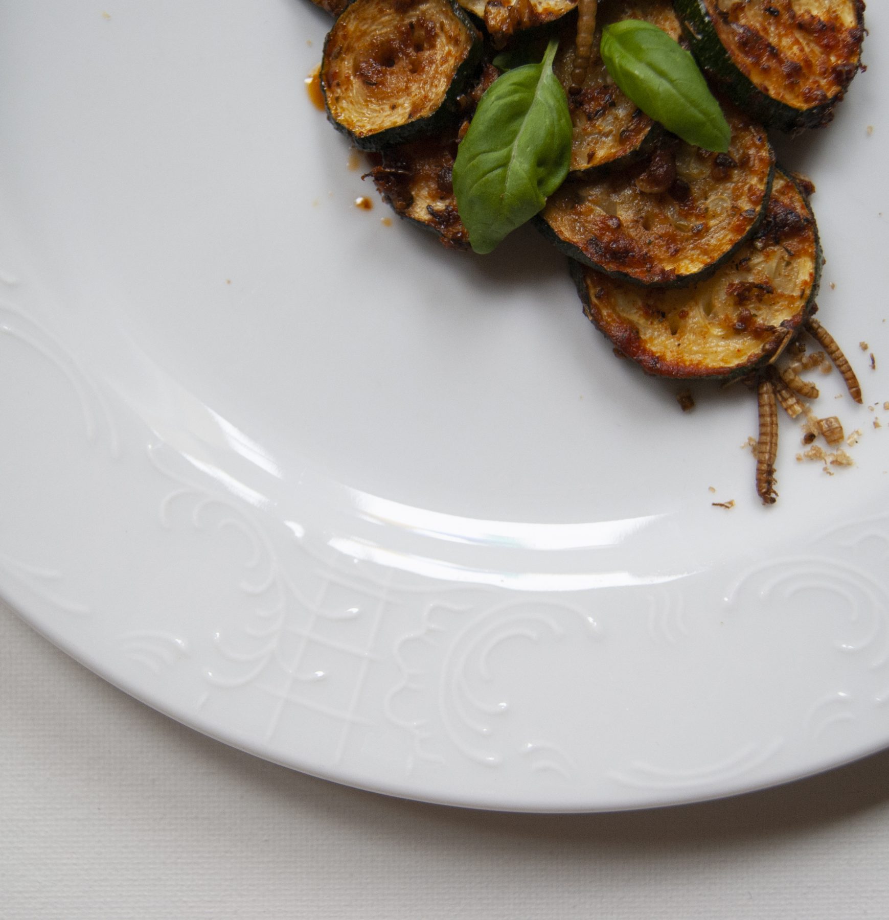 a dish with zucchini and insects on a white plate